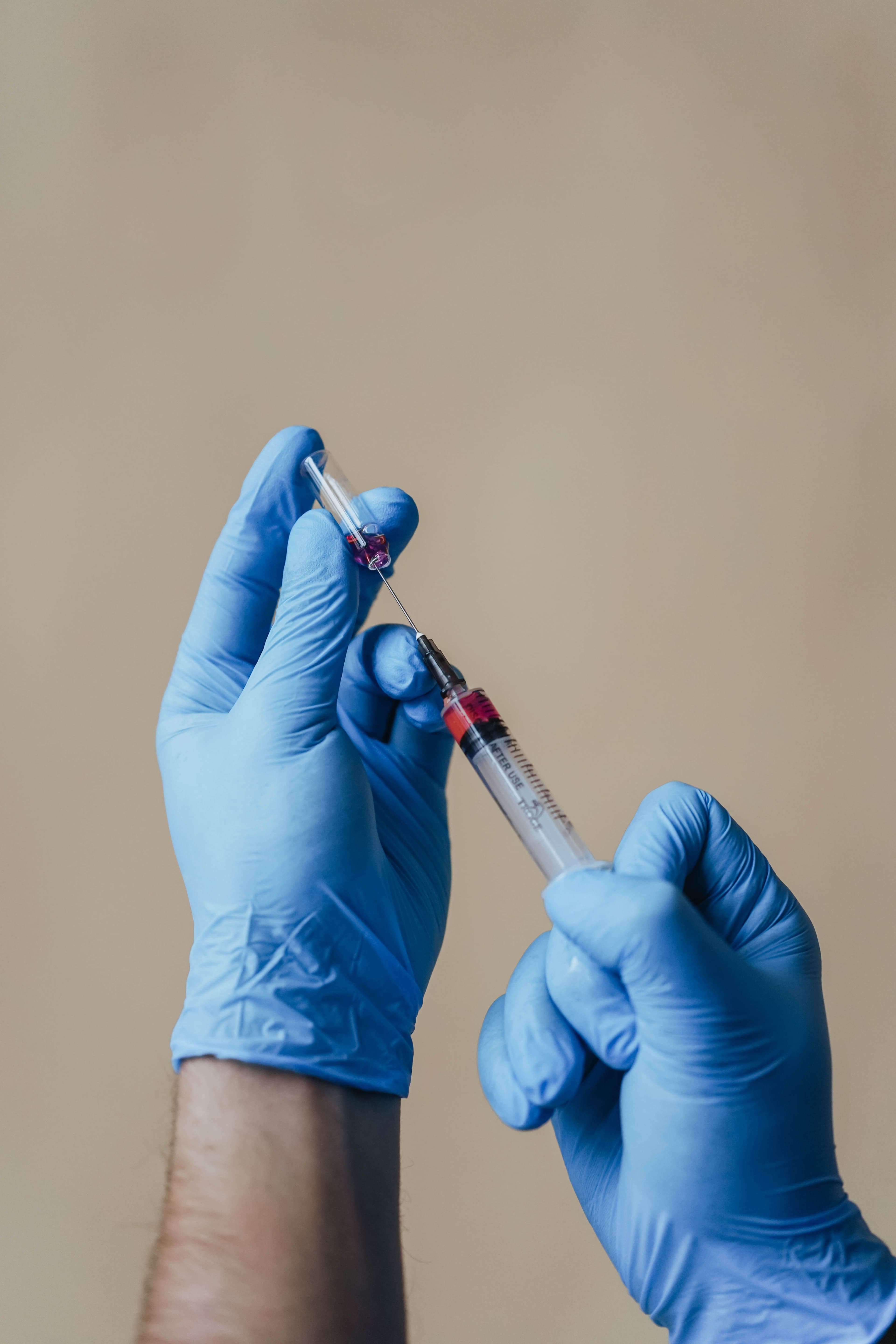 Gloved hands drawing medication from a vial into a syringe for an injection