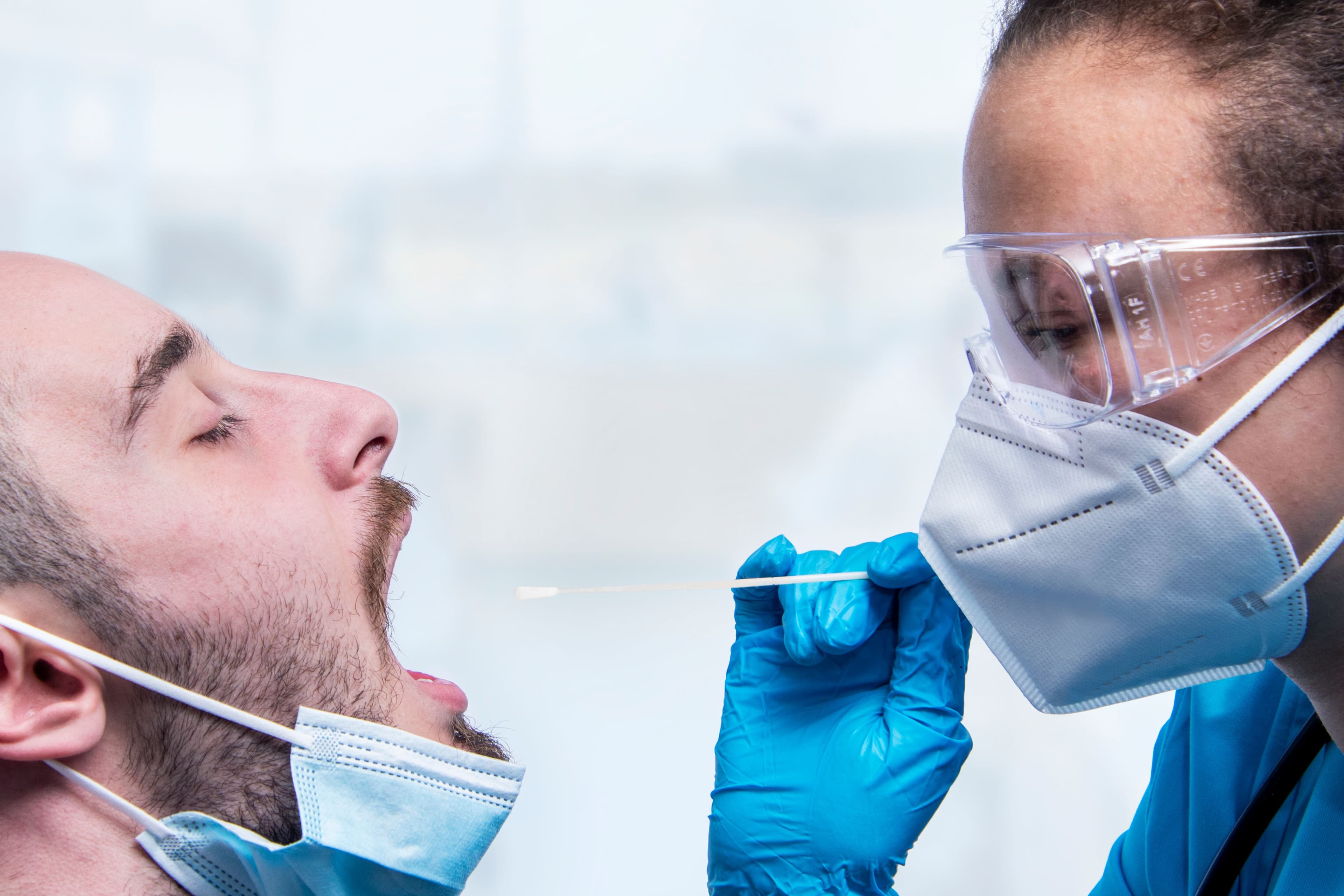 Provider in a mask and goggles swabbing a patient's throat for a flu, strep or COVID-19 test