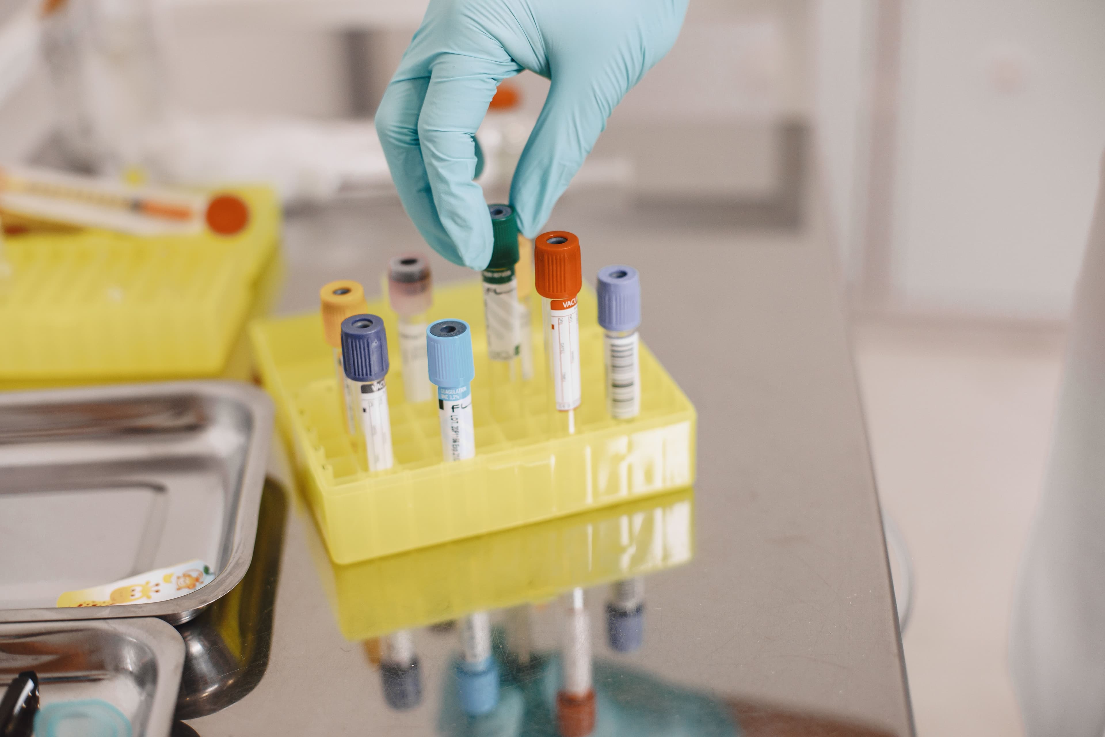 Gloved hand placing color-capped blood sample tubes in a rack for lab testing