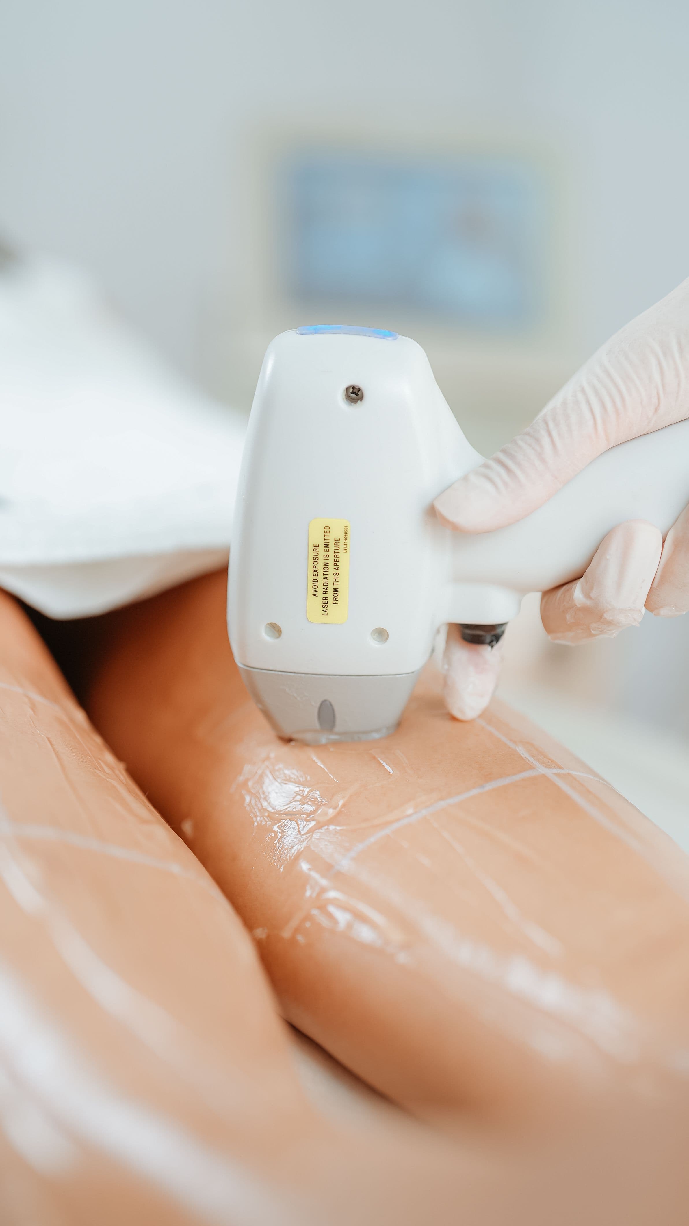 Gloved hand moving a handheld device over gel-covered skin